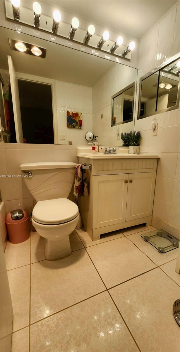 bathroom featuring tile patterned flooring, vanity, toilet, and tile walls