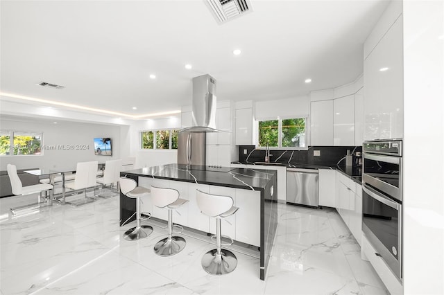 kitchen with white cabinets, appliances with stainless steel finishes, island range hood, and a healthy amount of sunlight