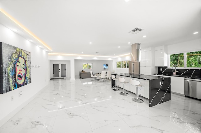 kitchen with island range hood, appliances with stainless steel finishes, a kitchen island, white cabinetry, and a breakfast bar area