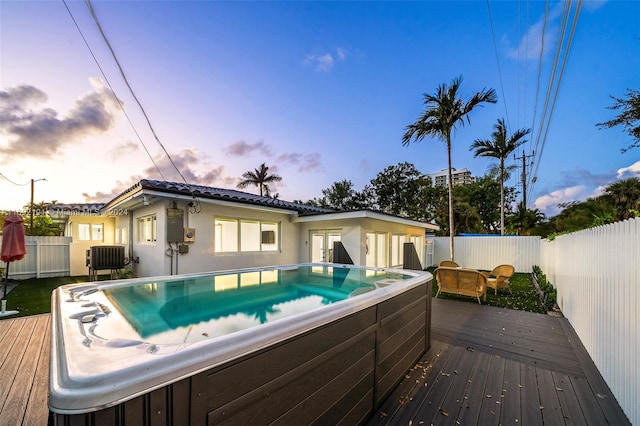 pool at dusk with a wooden deck and a hot tub