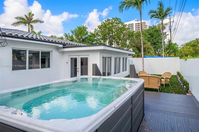 view of swimming pool with french doors, a hot tub, and a deck