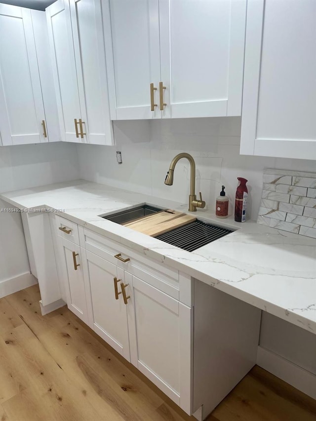 kitchen featuring light stone countertops, sink, light hardwood / wood-style flooring, backsplash, and white cabinets