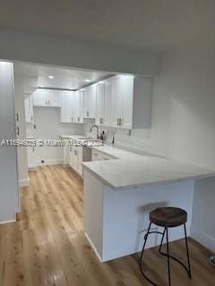 kitchen featuring kitchen peninsula, a breakfast bar, white cabinets, and light hardwood / wood-style flooring