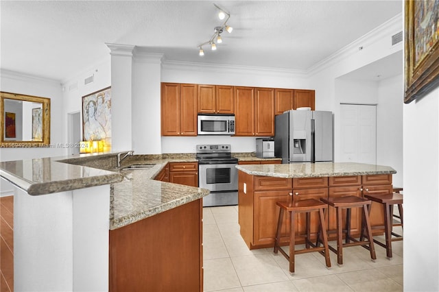 kitchen with a kitchen bar, kitchen peninsula, light stone counters, stainless steel appliances, and sink