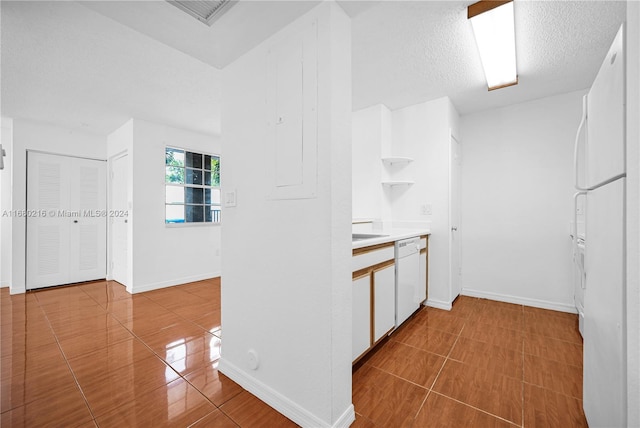 kitchen with tile patterned floors, white cabinets, white dishwasher, and a textured ceiling