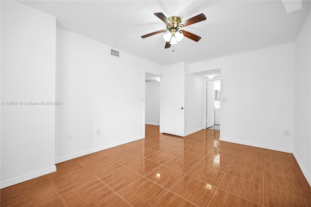 tiled empty room with ceiling fan and a textured ceiling