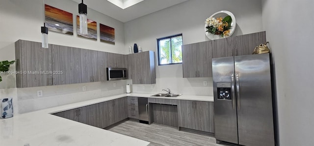 kitchen with stainless steel appliances, sink, a towering ceiling, light wood-type flooring, and backsplash