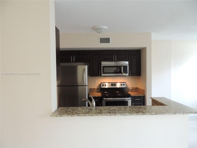 kitchen featuring kitchen peninsula, light stone counters, stainless steel appliances, and a textured ceiling