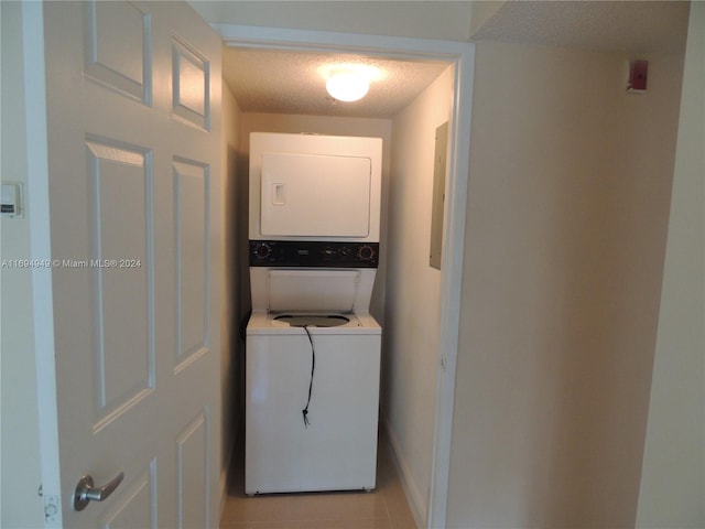 laundry room featuring a textured ceiling, light tile patterned flooring, and stacked washer / drying machine