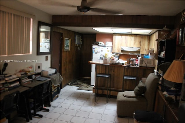 kitchen with kitchen peninsula, a kitchen bar, white fridge, and wood walls