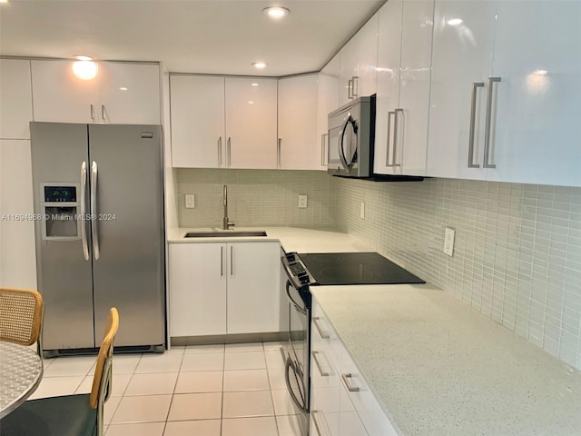 kitchen with sink, tasteful backsplash, light tile patterned flooring, white cabinetry, and stainless steel appliances