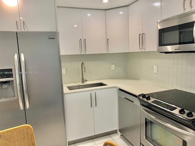 kitchen featuring backsplash, stainless steel appliances, sink, white cabinets, and light tile patterned flooring