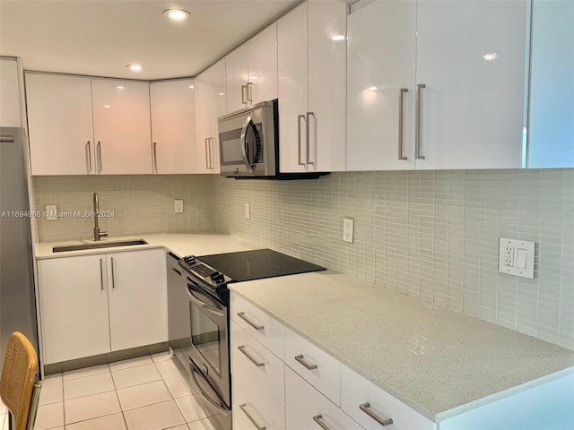 kitchen with light stone countertops, appliances with stainless steel finishes, sink, light tile patterned floors, and white cabinets