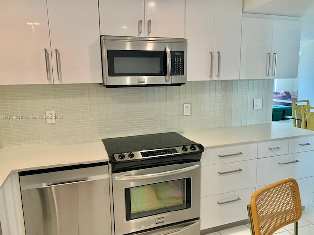 kitchen with backsplash, white cabinetry, light tile patterned floors, and stainless steel appliances