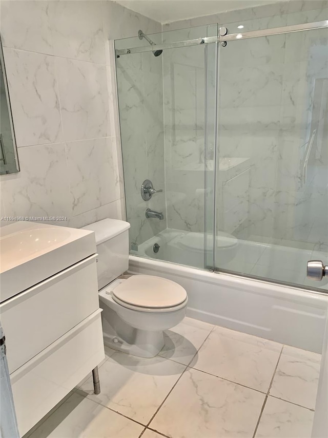 full bathroom with shower / bath combination with glass door, vanity, toilet, and tile walls