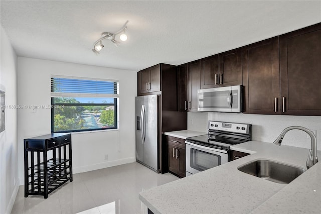 kitchen featuring dark brown cabinetry, light stone countertops, sink, stainless steel appliances, and a textured ceiling