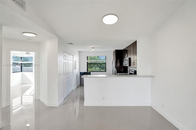 kitchen with dark brown cabinets, light tile patterned flooring, kitchen peninsula, and stainless steel appliances