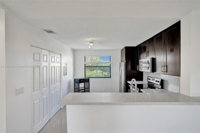 kitchen featuring dark brown cabinetry, kitchen peninsula, and stainless steel appliances