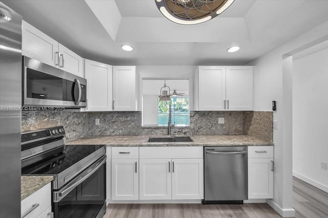 kitchen with appliances with stainless steel finishes, white cabinets, light stone counters, and sink