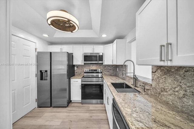 kitchen with light stone countertops, appliances with stainless steel finishes, white cabinetry, sink, and a raised ceiling