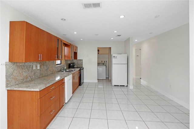 kitchen featuring sink, tasteful backsplash, light stone counters, washer / clothes dryer, and white appliances