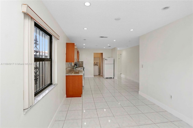 kitchen featuring light tile patterned flooring, a textured ceiling, white fridge, light stone counters, and washer / clothes dryer