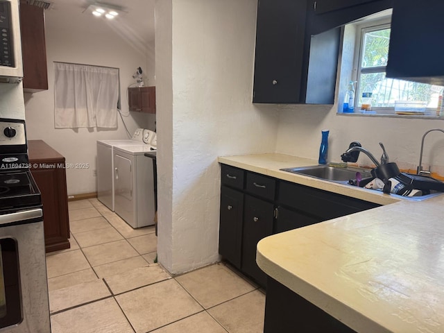 kitchen with stainless steel range oven, sink, light tile patterned floors, and washing machine and clothes dryer