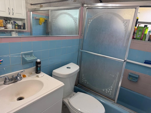 full bathroom with toilet, tile walls, vanity, enclosed tub / shower combo, and decorative backsplash