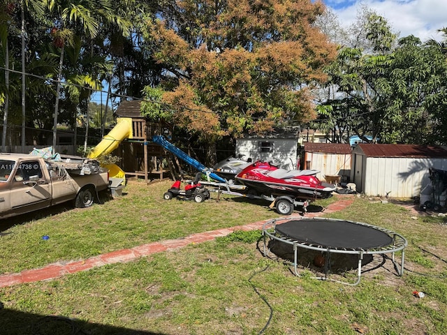 view of yard featuring a trampoline, a playground, and a storage unit