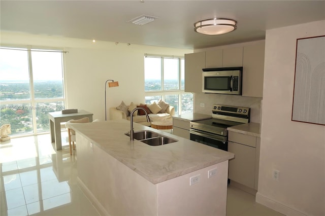 kitchen with sink, backsplash, an island with sink, light tile patterned floors, and appliances with stainless steel finishes