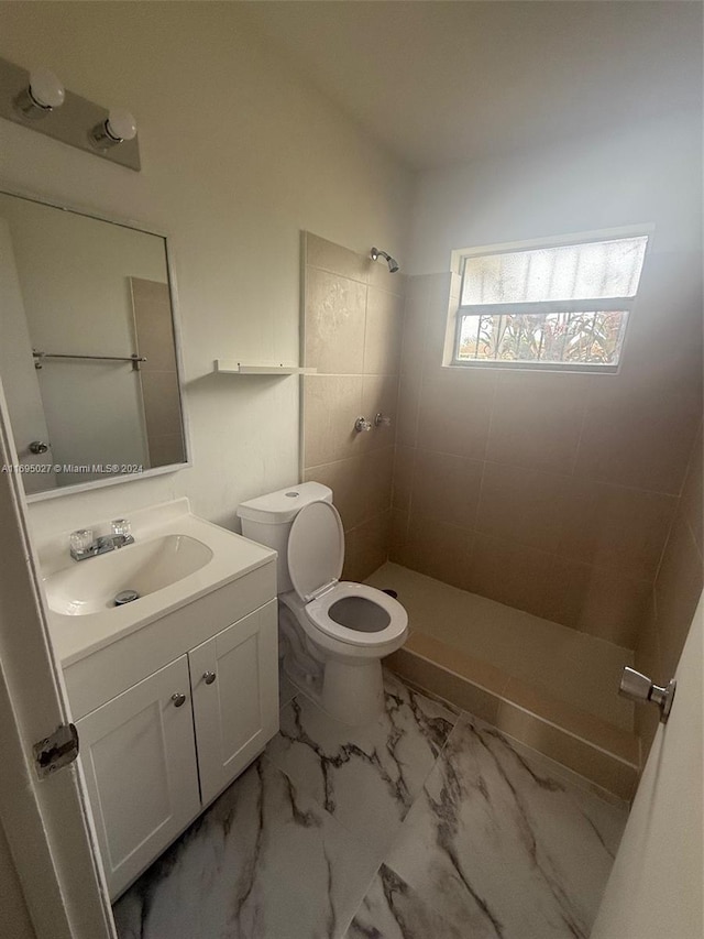 bathroom featuring a tile shower, vanity, and toilet