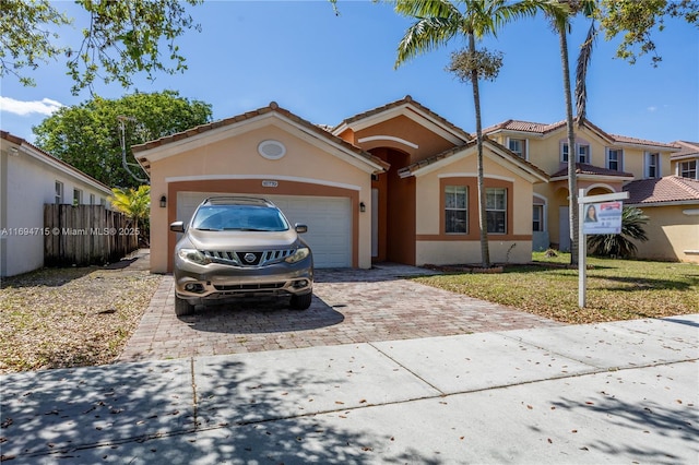 mediterranean / spanish-style home featuring driveway, stucco siding, fence, a tiled roof, and a garage