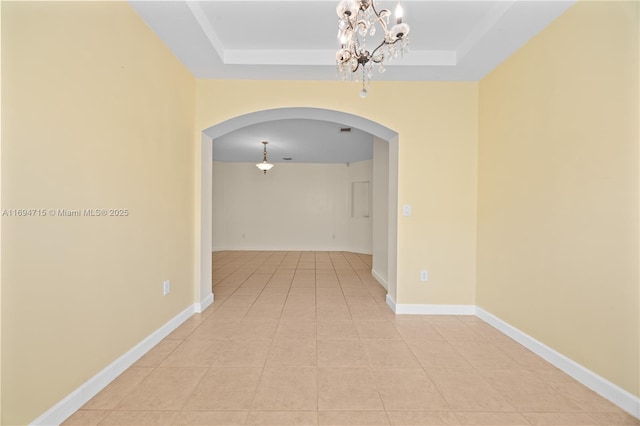 unfurnished room featuring arched walkways, baseboards, light tile patterned flooring, and a raised ceiling