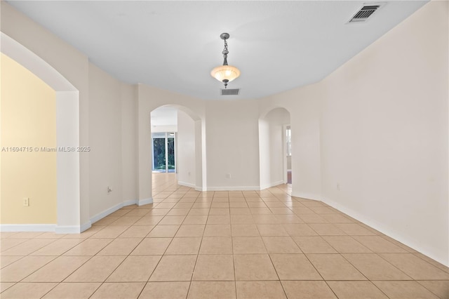 unfurnished room with light tile patterned flooring, baseboards, arched walkways, and visible vents