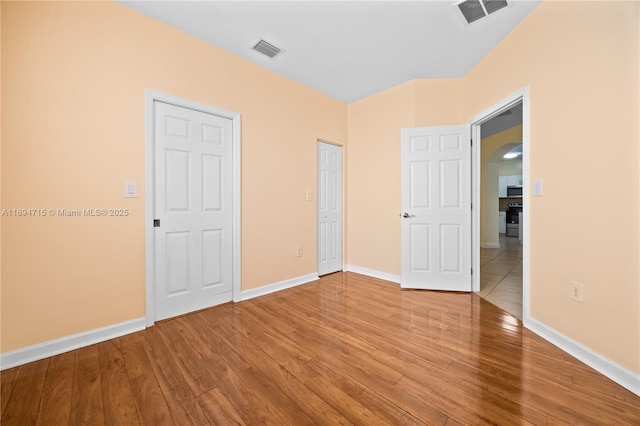 unfurnished bedroom with wood finished floors, arched walkways, and visible vents