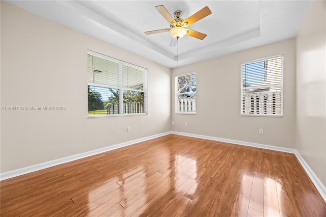 spare room featuring a ceiling fan, a raised ceiling, baseboards, and light wood-type flooring