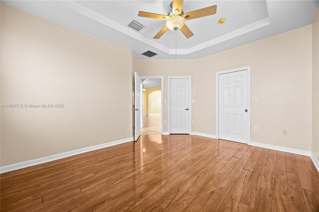 unfurnished bedroom featuring a tray ceiling, baseboards, visible vents, and wood finished floors