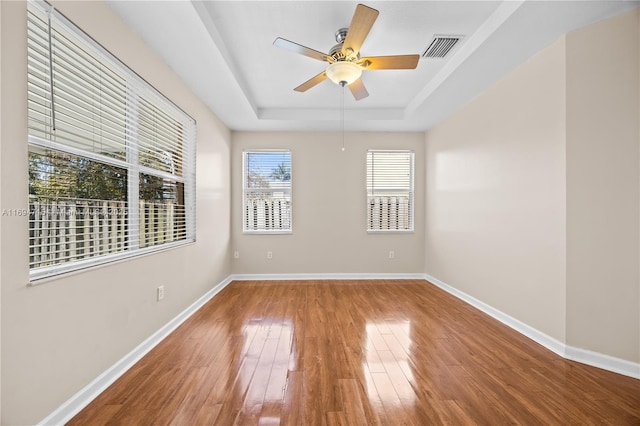 unfurnished room with visible vents, baseboards, a ceiling fan, a raised ceiling, and wood-type flooring