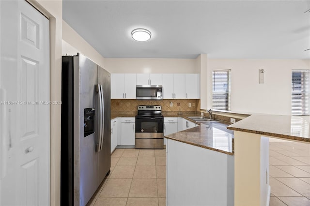 kitchen with a sink, white cabinetry, appliances with stainless steel finishes, a peninsula, and light tile patterned floors