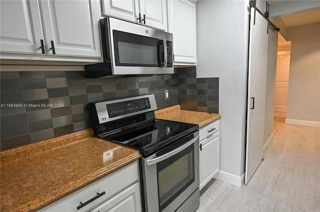 kitchen with backsplash, stainless steel appliances, a barn door, light hardwood / wood-style flooring, and white cabinetry