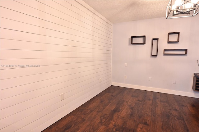 unfurnished room featuring wood walls, dark wood-type flooring, a textured ceiling, and a notable chandelier