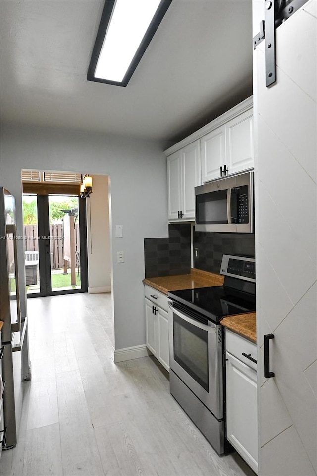 kitchen featuring appliances with stainless steel finishes, a barn door, light hardwood / wood-style floors, and white cabinetry