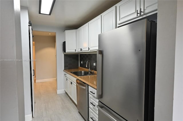 kitchen featuring decorative backsplash, appliances with stainless steel finishes, sink, white cabinets, and light hardwood / wood-style floors