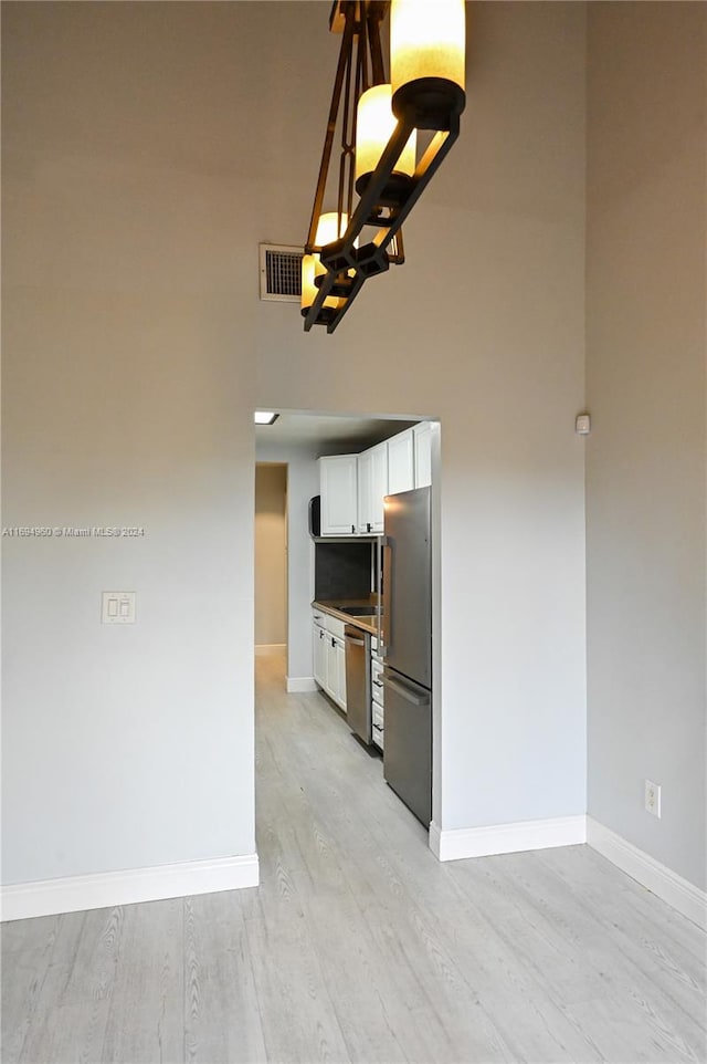 kitchen featuring a high ceiling, white cabinets, light hardwood / wood-style flooring, decorative light fixtures, and stainless steel appliances