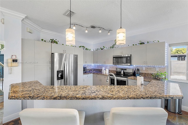 kitchen featuring kitchen peninsula, appliances with stainless steel finishes, a kitchen bar, and ornamental molding