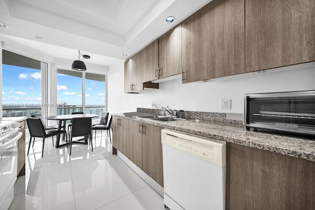 kitchen with sink, a raised ceiling, stone countertops, white appliances, and light tile patterned floors