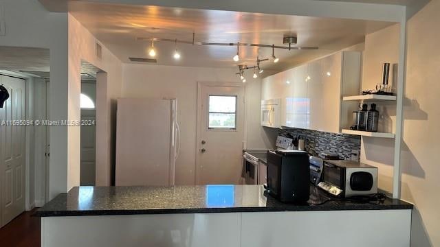 kitchen featuring track lighting, tasteful backsplash, stainless steel appliances, dark stone countertops, and white cabinetry