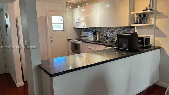 kitchen with sink, kitchen peninsula, decorative backsplash, white cabinets, and appliances with stainless steel finishes