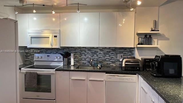 kitchen with decorative backsplash, dark stone counters, white appliances, sink, and white cabinets