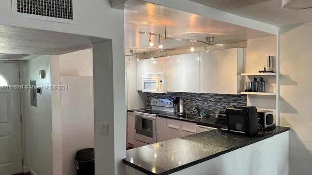 kitchen featuring white cabinetry, sink, dark stone counters, electric stove, and decorative backsplash